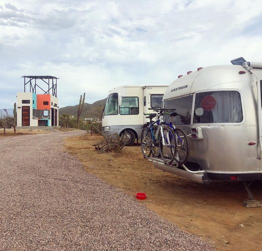 Motorhome and motorcycle parked at a desert campground with the ocean in the distance